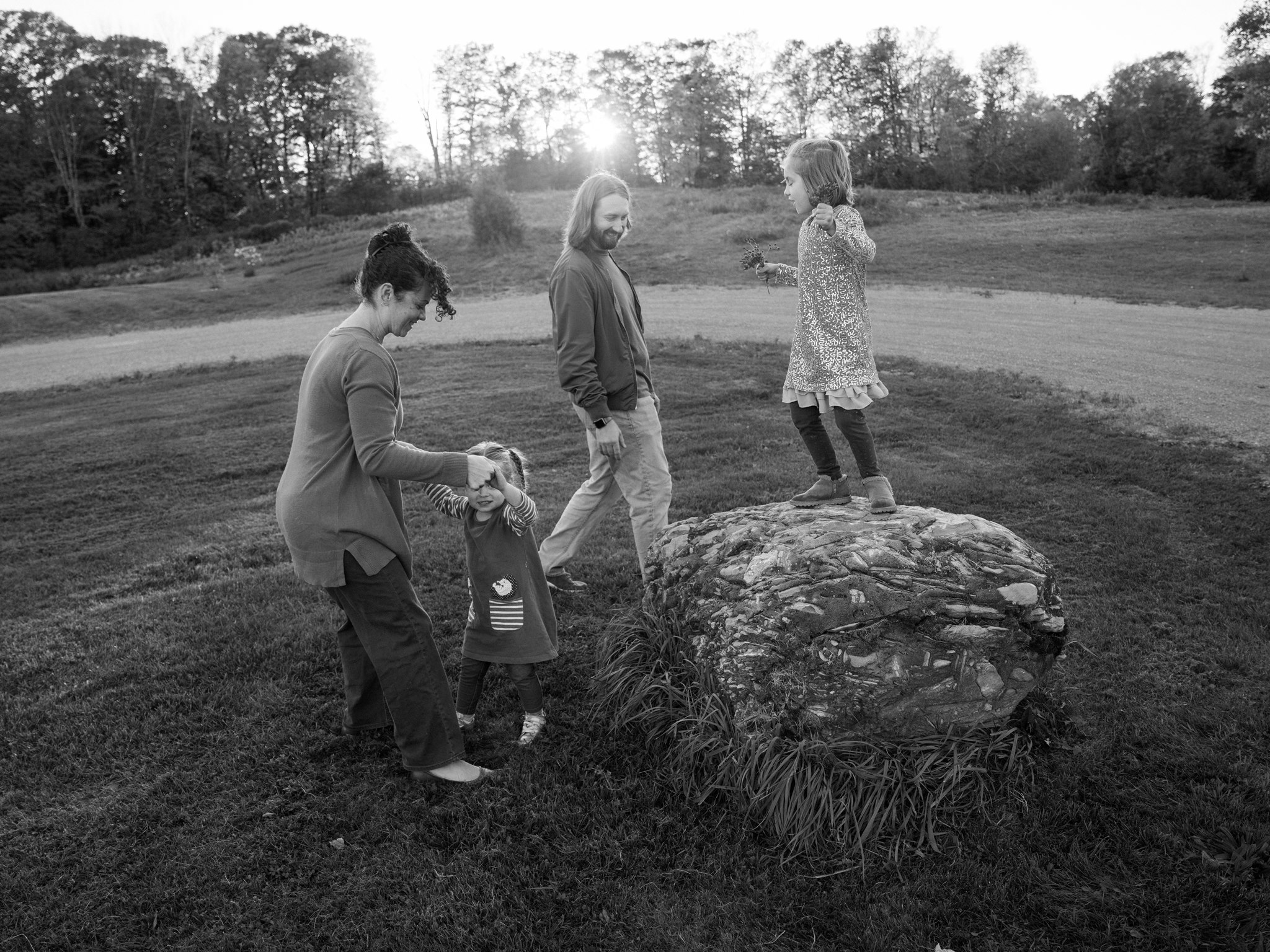 Black and white family scene with children exploring around a rock